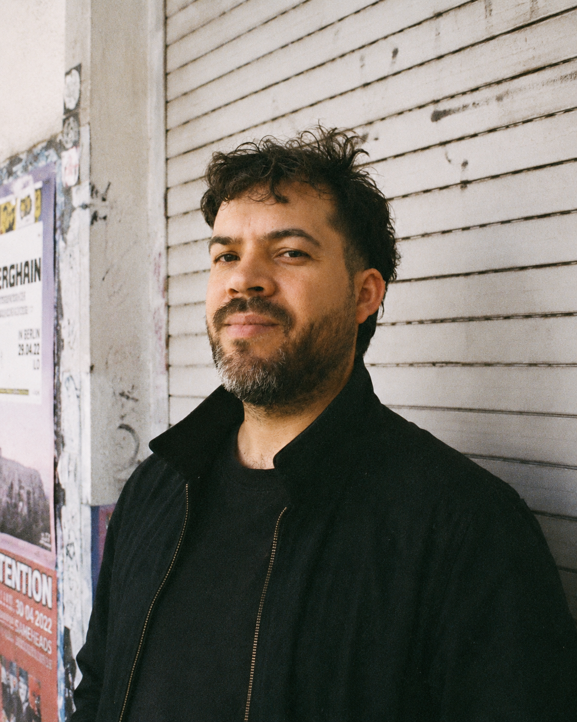 Portrait of Sebastián Saavedra in front of a shuttered storefront in Berlin